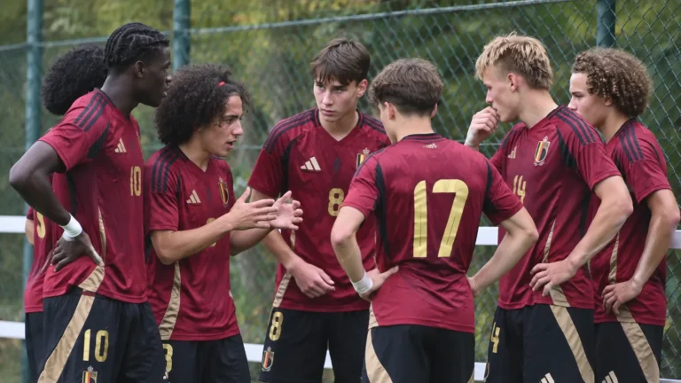 Een groep jonge voetballers in donkerrode Belgische tenues staat samen langs het veld.