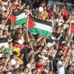 Supporters op de tribunes houden Palestijnse vlaggen omhoog tijdens een solidariteitsactie.