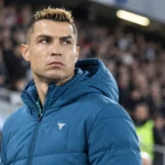 Cristiano Ronaldo in een blauwe Portugal-jas aan de rand van een stadion.