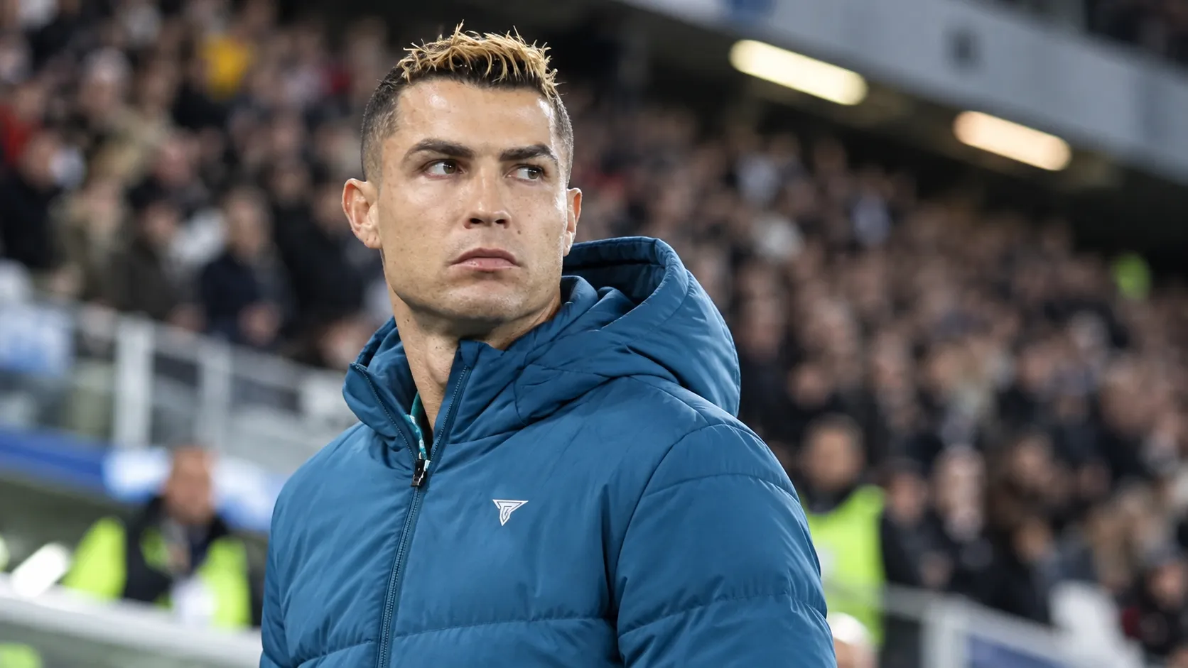 Cristiano Ronaldo in een blauwe Portugal-jas aan de rand van een stadion.