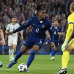 Een Franse veldspeler in donkerblauw tijdens een wedstrijdmoment tegen Belgische spelers op een vol stadion.