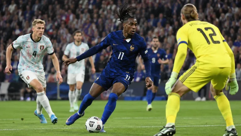 Een Franse veldspeler in donkerblauw tijdens een wedstrijdmoment tegen Belgische spelers op een vol stadion.