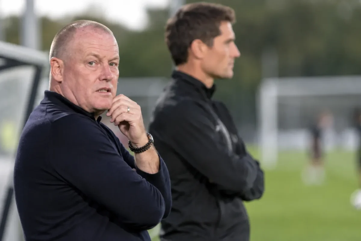 Twee leden van de technische staf bekijken een training naast het veld.
