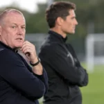 Twee leden van de technische staf bekijken een training naast het veld.