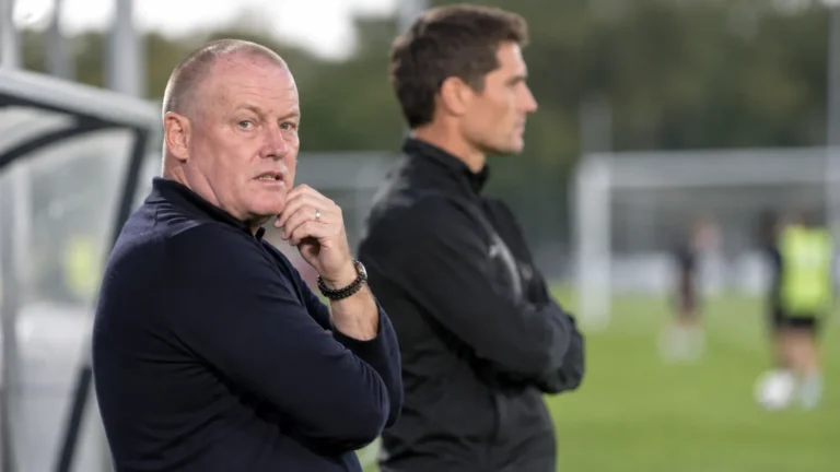 Twee leden van de technische staf bekijken een training naast het veld.