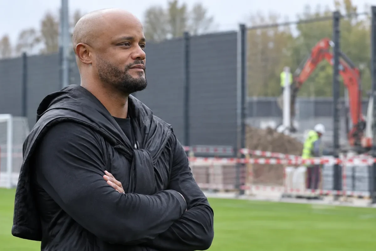 Vincent Kompany aan de rand van een trainingsveld bij een bouwzone met nieuwe afscherming.