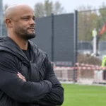 Vincent Kompany aan de rand van een trainingsveld bij een bouwzone met nieuwe afscherming.