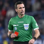 Erik Lambrechts als scheidsrechter met een rode kaart tijdens een voetbalwedstrijd.