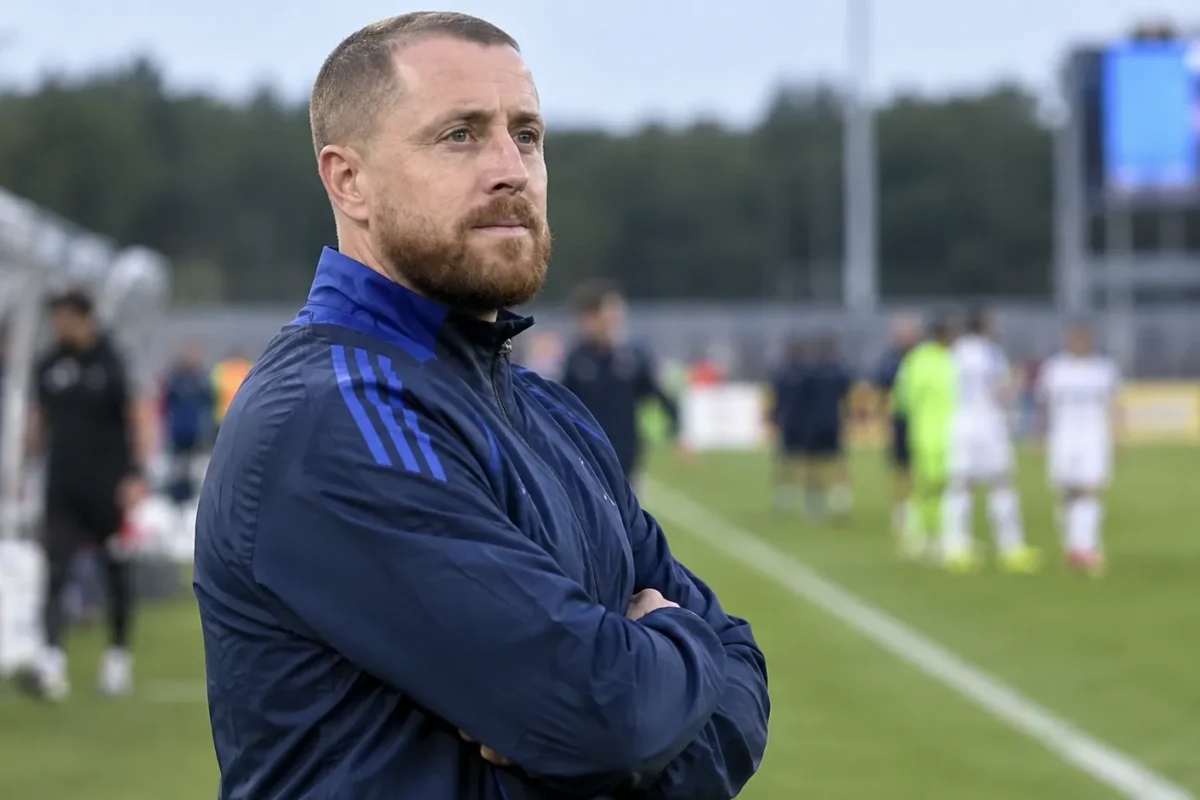 Een Belgische jeugdcoach in blauwe trainingskleding langs de zijlijn na een wedstrijd.