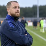 Een Belgische jeugdcoach in blauwe trainingskleding langs de zijlijn na een wedstrijd.