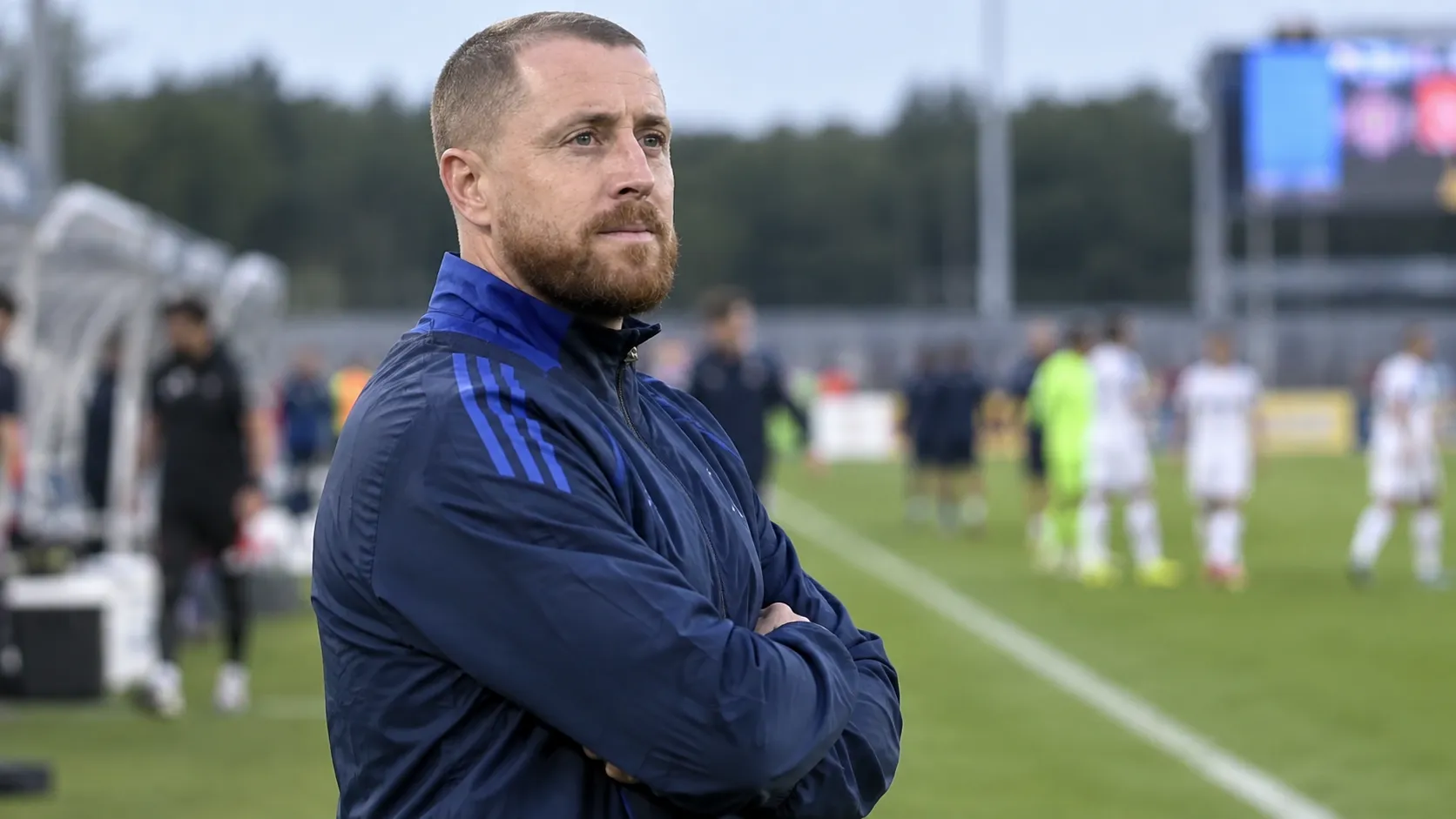 Een Belgische jeugdcoach in blauwe trainingskleding langs de zijlijn na een wedstrijd.