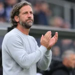 Rik De Mil applaudisseert langs de zijlijn in een stadion.
