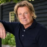 Hans Kraay junior in een nieuwe buitenportretfoto bij een donker houten gebouw.