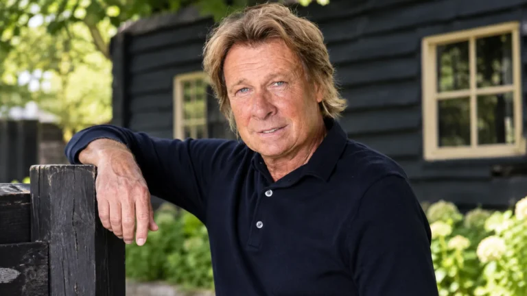 Hans Kraay junior in een nieuwe buitenportretfoto bij een donker houten gebouw.