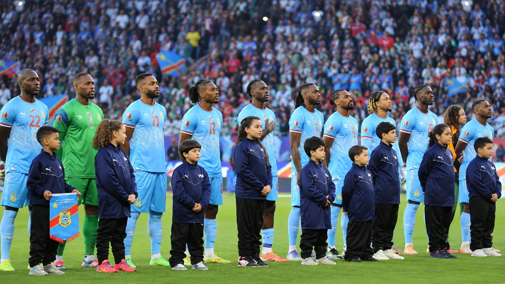 Spelers van Congo staan opgesteld voor een interland met jeugdmascottes voor hen.