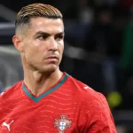 Een speler van Portugal in een rood shirt kijkt opzij in een stadion.