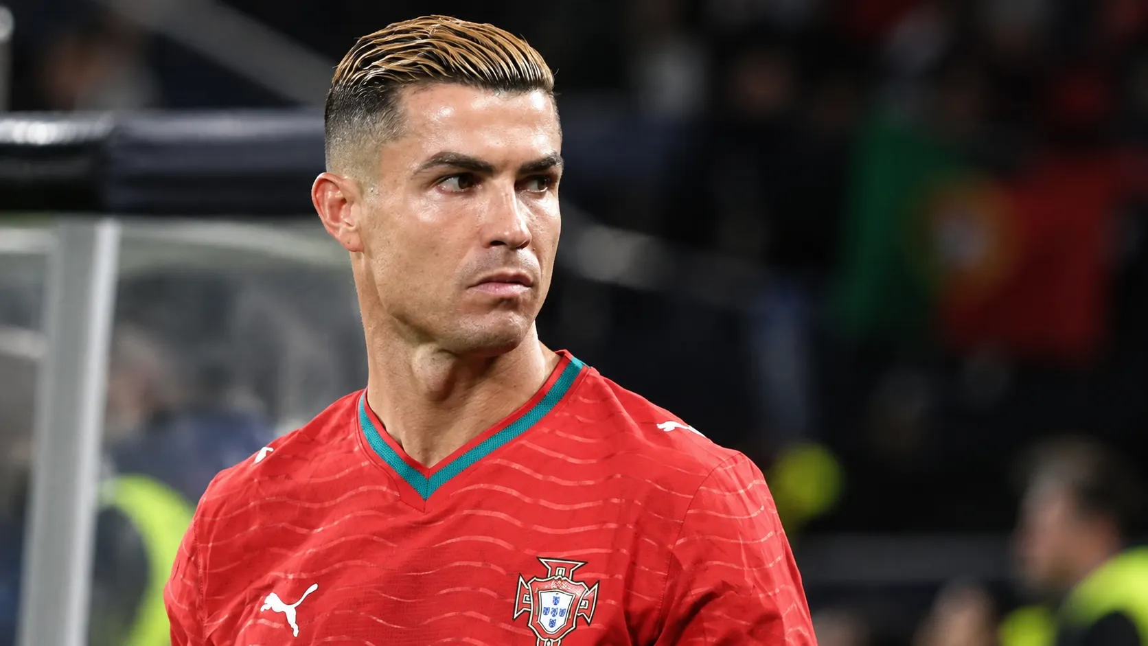 Een speler van Portugal in een rood shirt kijkt opzij in een stadion.