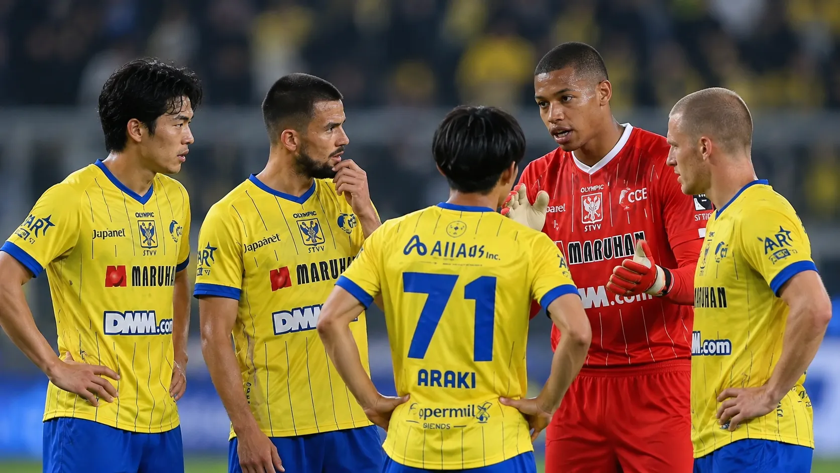 Voetballers in gele tenues en een doelman in rood verzamelen zich op het veld.