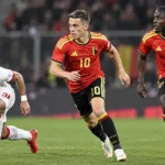 Drie voetballers in actie tijdens een wedstrijd van de Rode Duivels.
