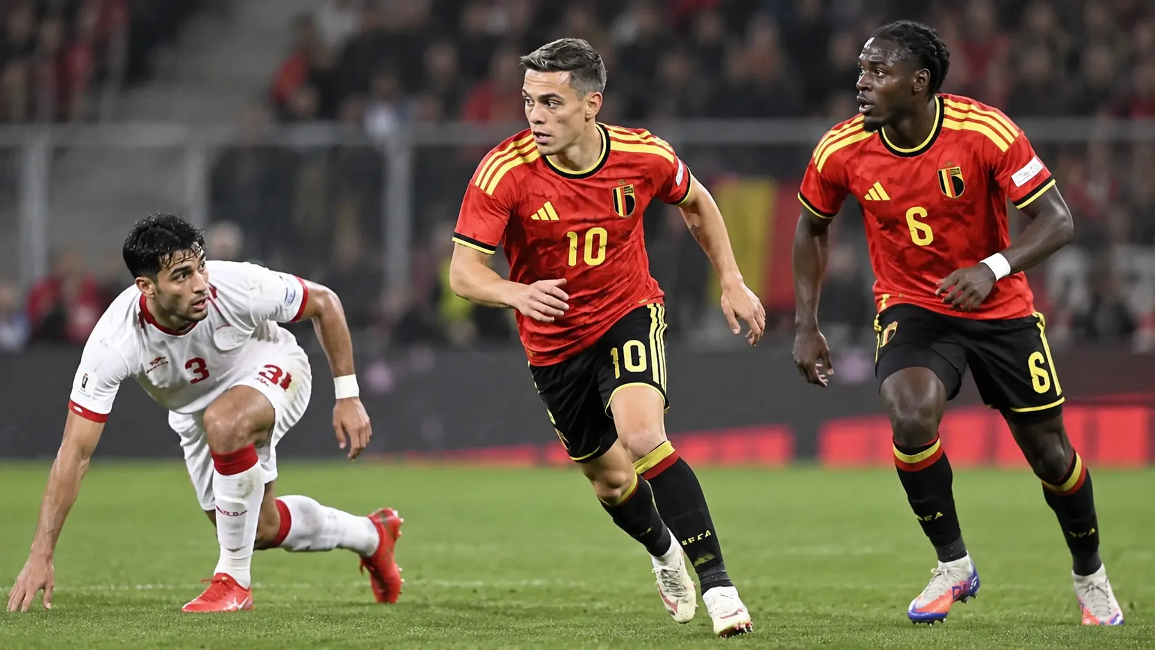 Drie voetballers in actie tijdens een wedstrijd van de Rode Duivels.