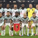 Een groep Belgische nationale spelers poseert met een wimpel op het veld van een verlicht stadion.