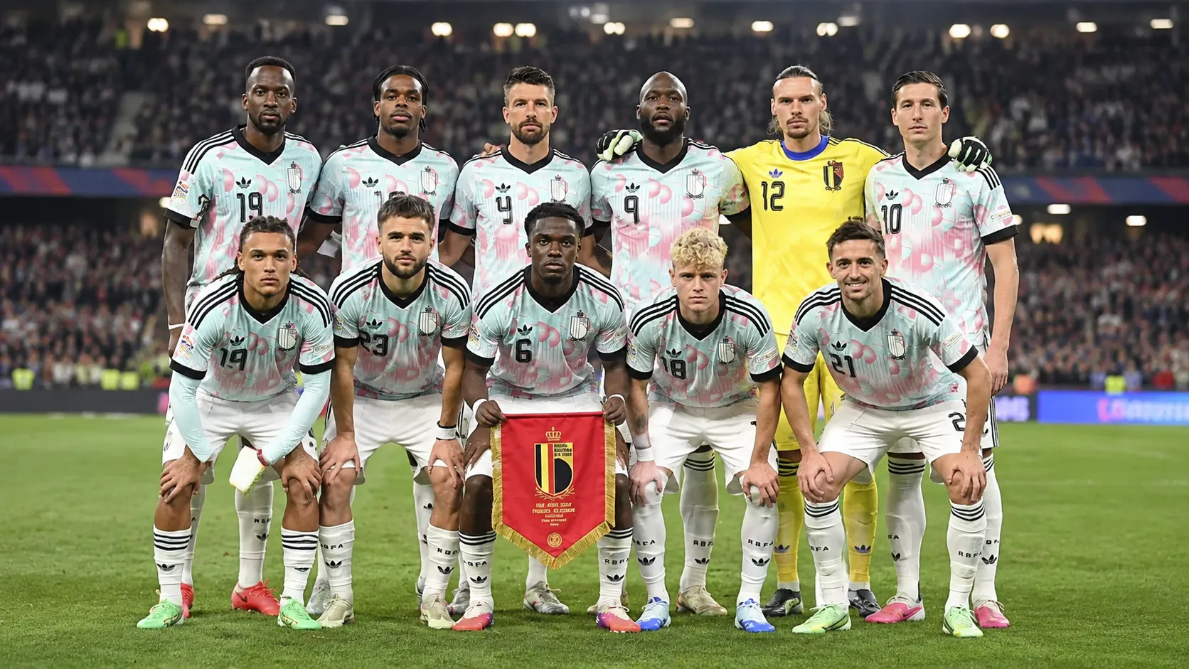 Een groep Belgische nationale spelers poseert met een wimpel op het veld van een verlicht stadion.