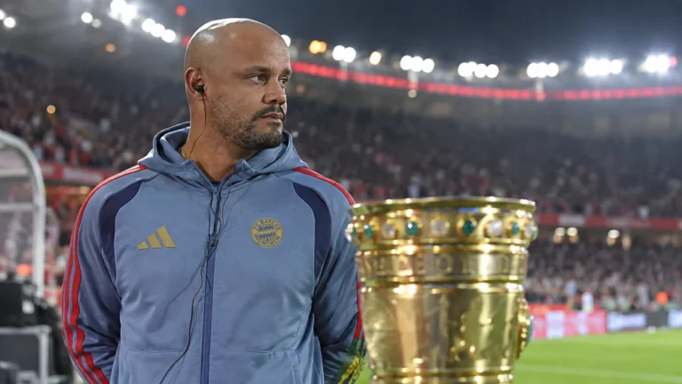 Een niet-spelende Bayern München-vertegenwoordiger staat naast een trofee aan de rand van het veld.
