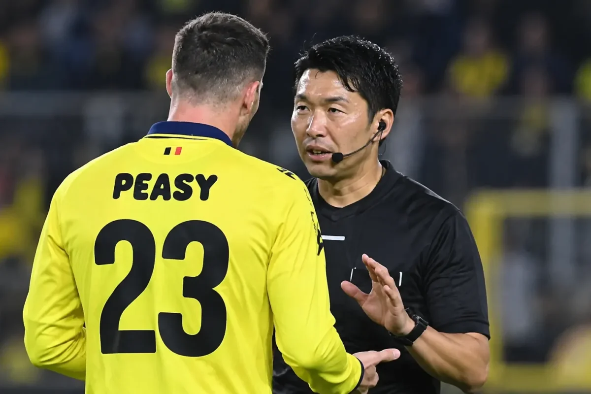 Een scheidsrechter spreekt op het veld met een speler in een geel tenue.