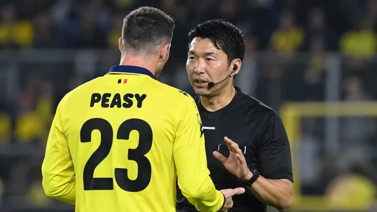 Een scheidsrechter spreekt op het veld met een speler in een geel tenue.