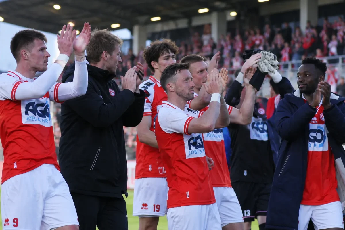 Een groep spelers en stafleden van KV Kortrijk applaudisseert richting de tribunes.