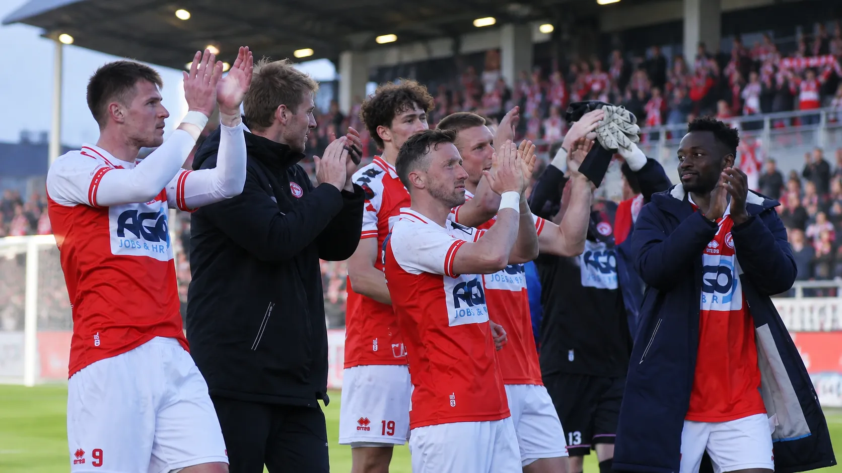 Een groep spelers en stafleden van KV Kortrijk applaudisseert richting de tribunes.