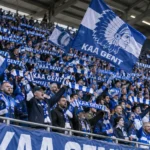 KAA Gent-supporters met blauwe en witte vlaggen op de tribune.