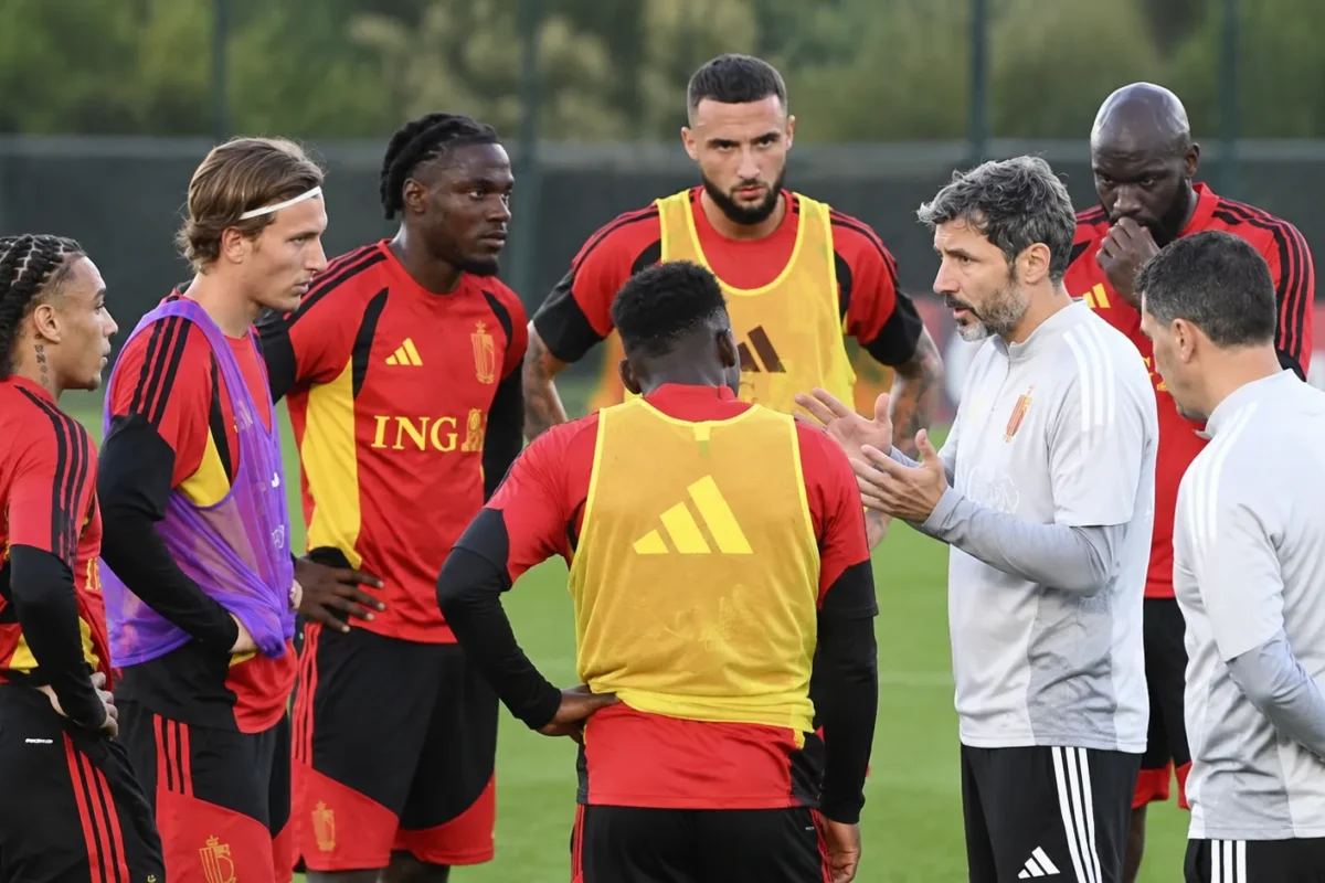Spelers en stafleden overleggen tijdens een trainingsmoment op een grasveld.