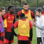 Spelers en stafleden overleggen tijdens een trainingsmoment op een grasveld.