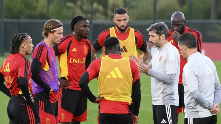 Spelers en stafleden overleggen tijdens een trainingsmoment op een grasveld.
