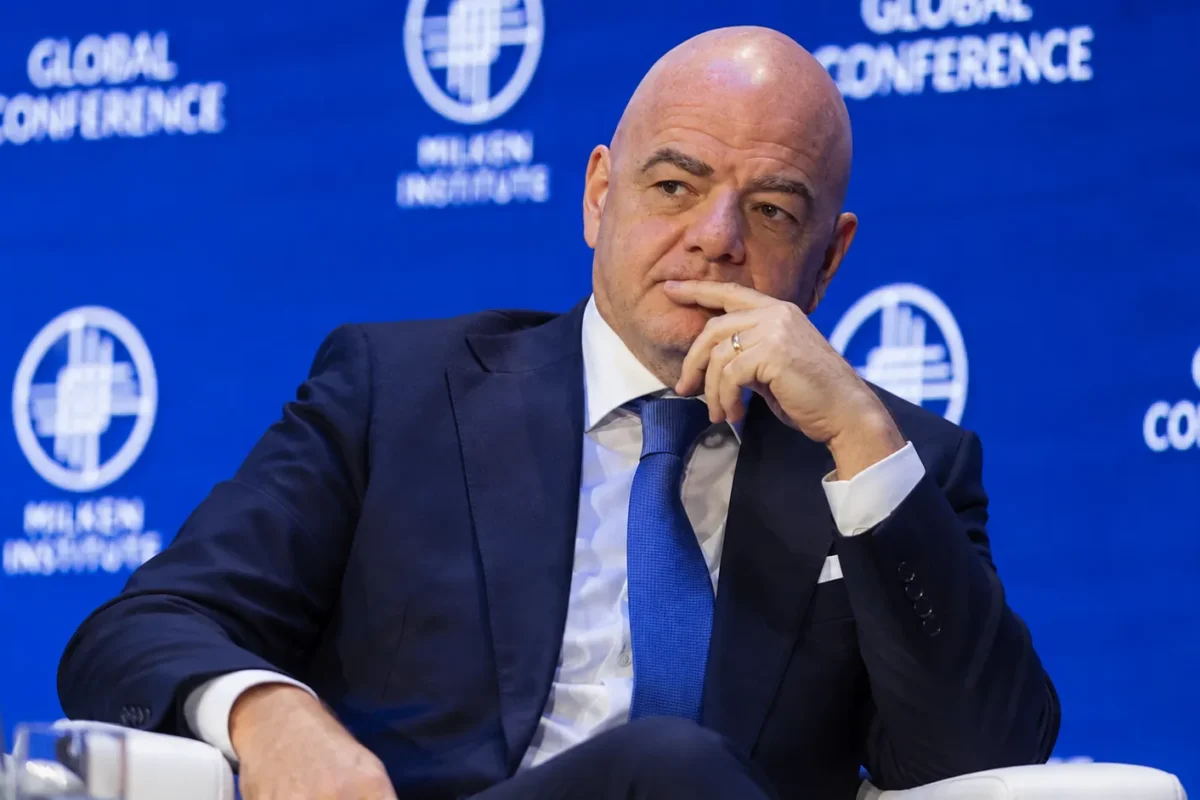 Een official in donker pak op een podium voor een blauw FIFA-conferentiedecor.