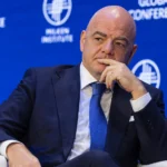Een official in donker pak op een podium voor een blauw FIFA-conferentiedecor.