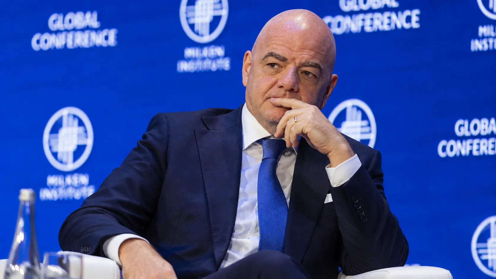 Een official in donker pak op een podium voor een blauw FIFA-conferentiedecor.