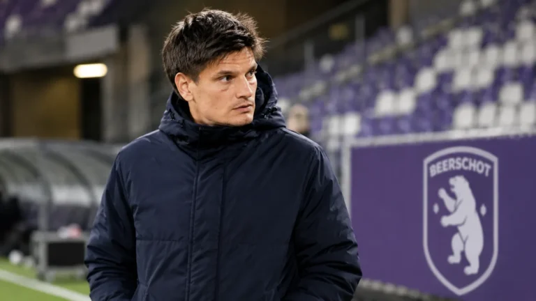 Jelle Vossen in een donkere jas langs de zijlijn van een Beerschot-stadion.