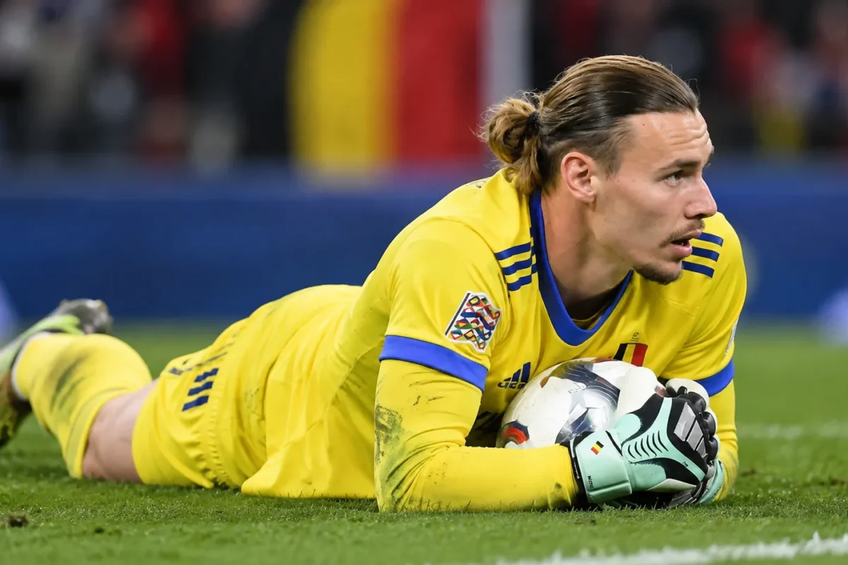 Maarten Vandevoordt in geel doelmanstenue met de bal na een lage redding op het veld.
