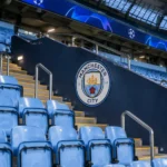 Lege tribune in het Etihad Stadium met een Manchester City-embleem aan de wand.