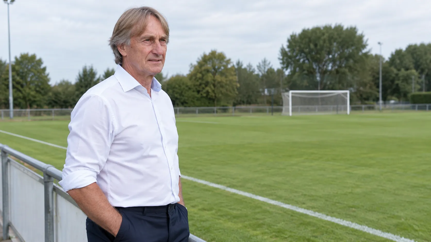 Adrie Koster kijkt naast een lokaal voetbalveld uit over het trainingsveld.