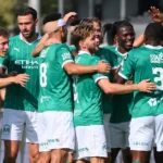 Een groep Lommel SK-spelers viert samen op het veld in groene tenues.