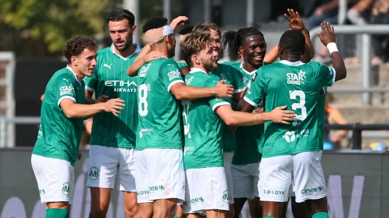 Een groep Lommel SK-spelers viert samen op het veld in groene tenues.
