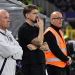 Niet-spelende mannen in de technische zone naast het voetbalveld.