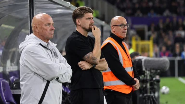 Niet-spelende mannen in de technische zone naast het voetbalveld.