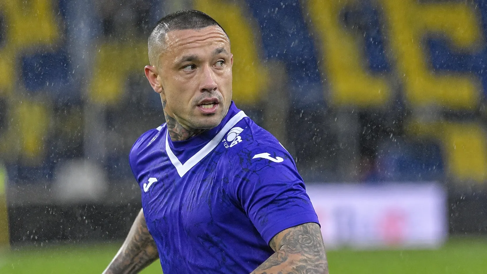 Radja Nainggolan in een paars voetbalshirt op een regenachtig veld.