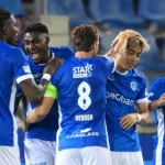 Een groep KRC Genk-spelers viert samen op het veld in blauwe shirts.