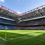 Leeg voetbalstadion met groen veld, tribunes en opvallende rode dakspanten.