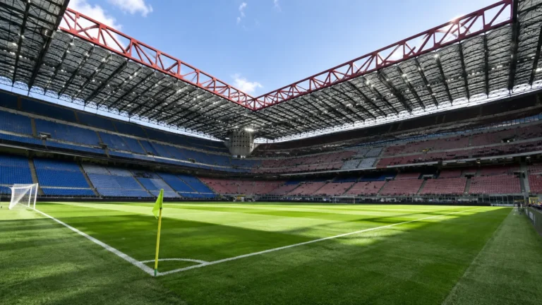 Leeg voetbalstadion met groen veld, tribunes en opvallende rode dakspanten.